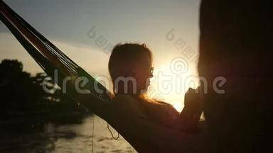 年轻女孩使用手机在吊床Silhuette与美丽的日落在海滩。 泰国Koh Phangan。 高清高清